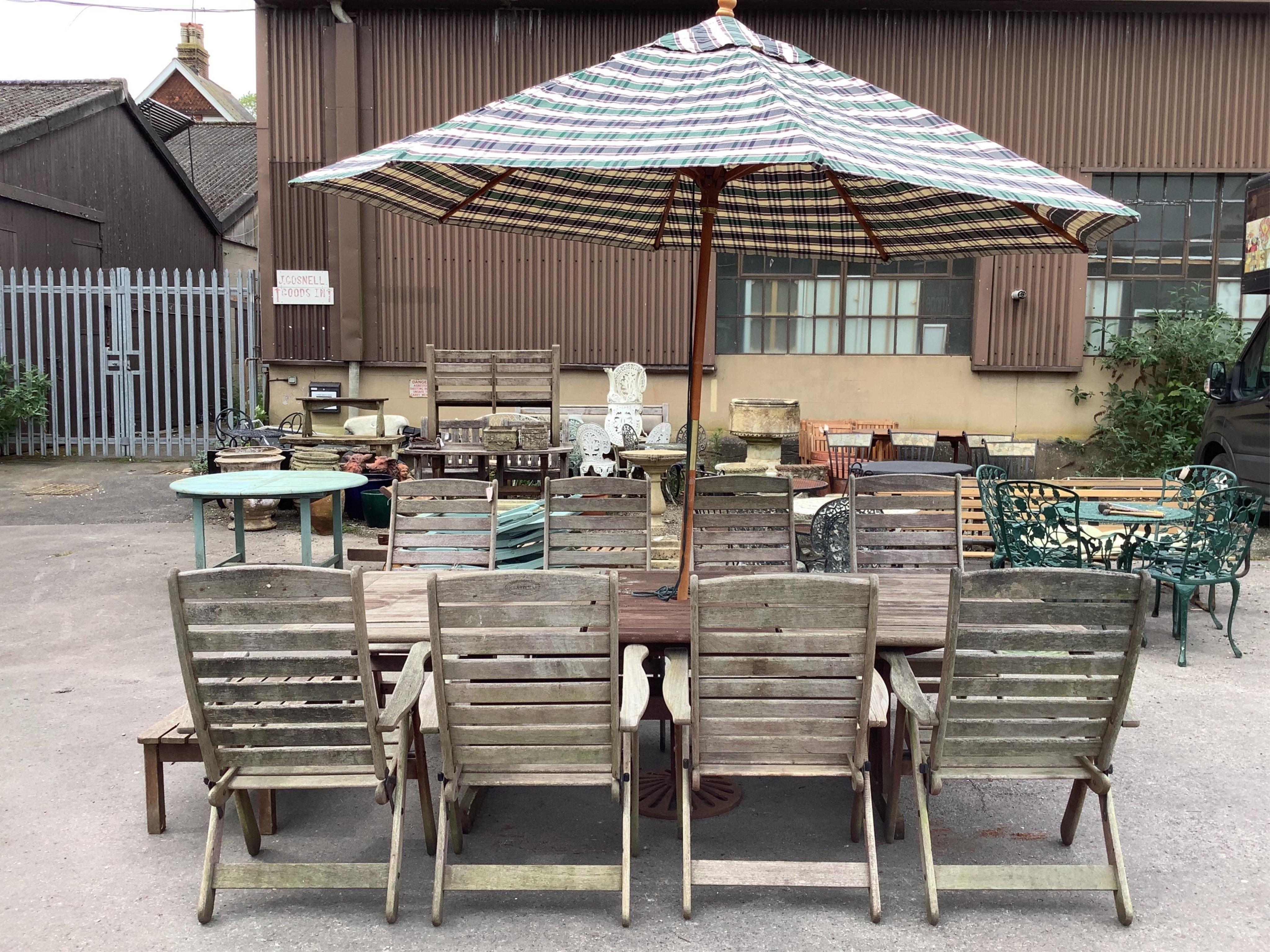 A large rectangular weathered teak extending garden table, width 256cm extended, depth 116cm, height 72cm together with a set of eight teak 'Clarecraft' elbow chairs, two with extending footrests, parasol, cast metal par